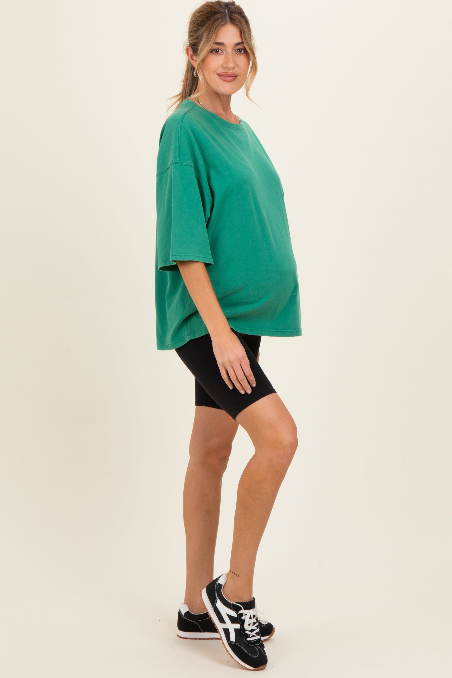 woman wearing a green oversized maternity t-shirt and black bike shorts, showcasing her baby bump