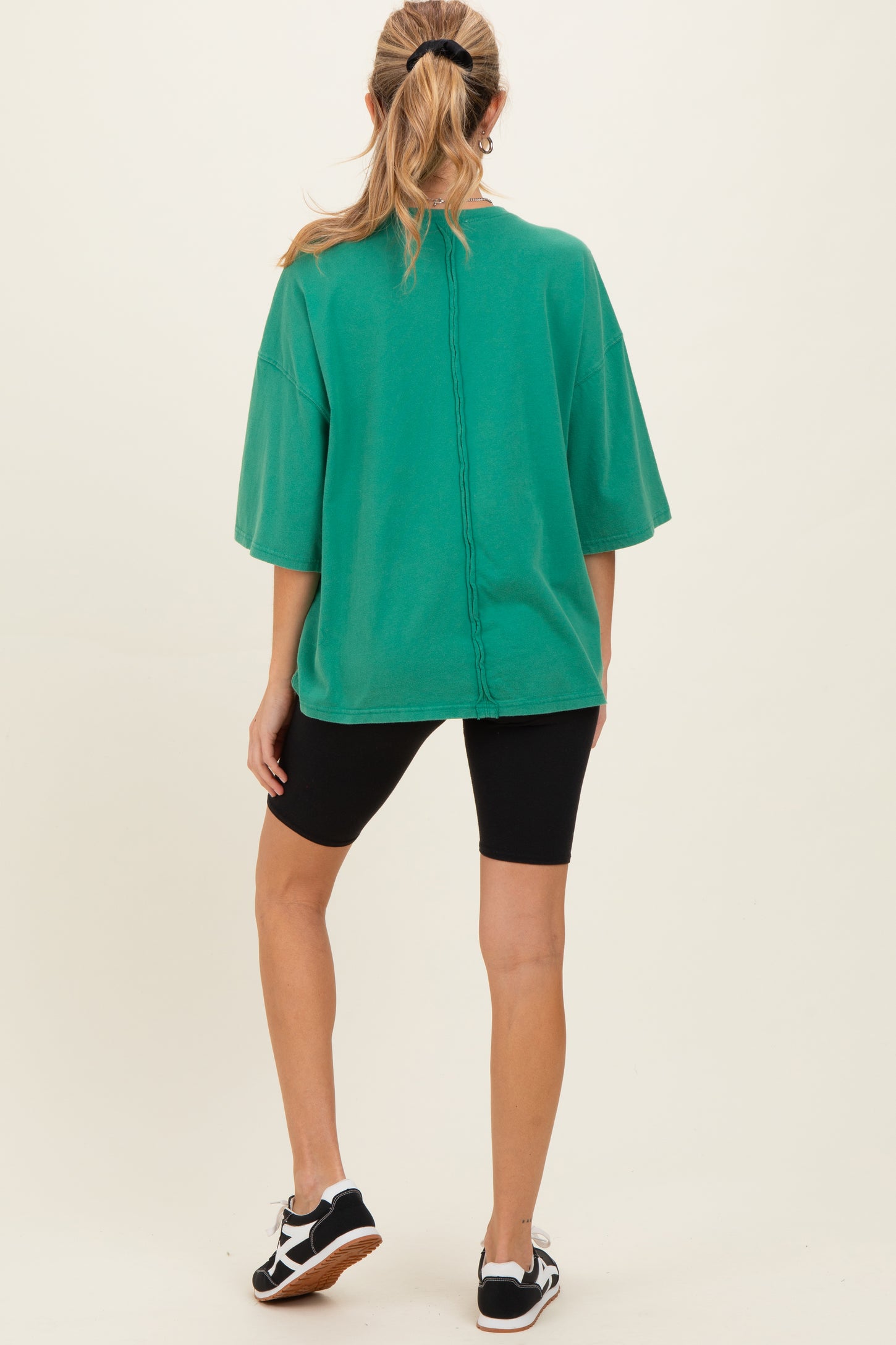 woman wearing a loose green maternity t-shirt with a seam detail on the back and black biker shorts