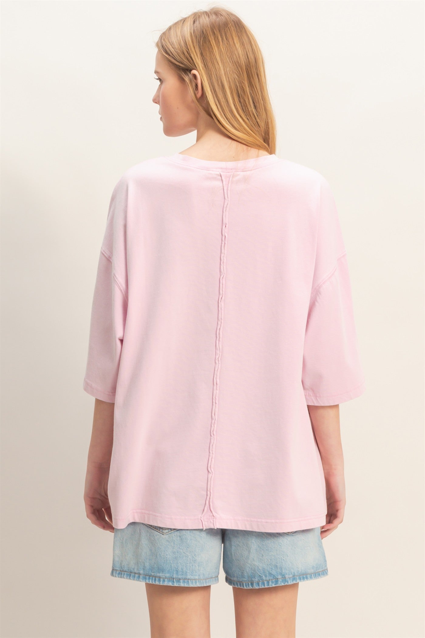 woman wearing a light pink oversized t-shirt with a back seam detail, paired with denim shorts