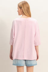 woman wearing a light pink oversized t-shirt with a back seam detail, paired with denim shorts