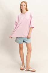 woman wearing an oversized pink t-shirt and distressed denim shorts, posing casually with one hand on the shirt