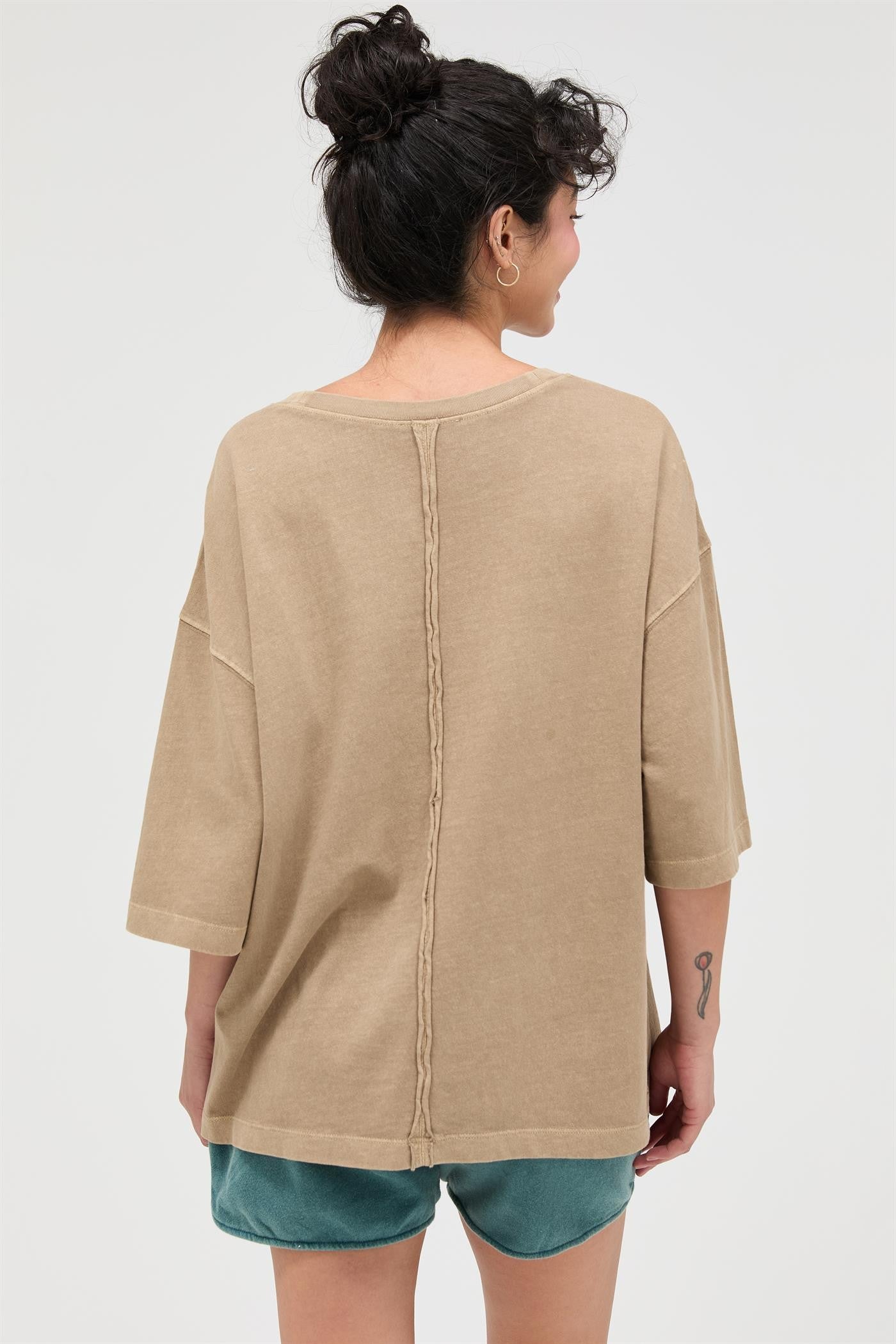 woman wearing a beige oversized t-shirt with a braided seam detail at the back, styled with teal shorts