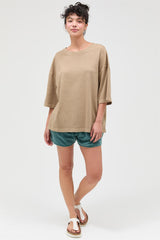woman wearing a brown oversized short sleeve top and green shorts, standing with one foot slightly forward
