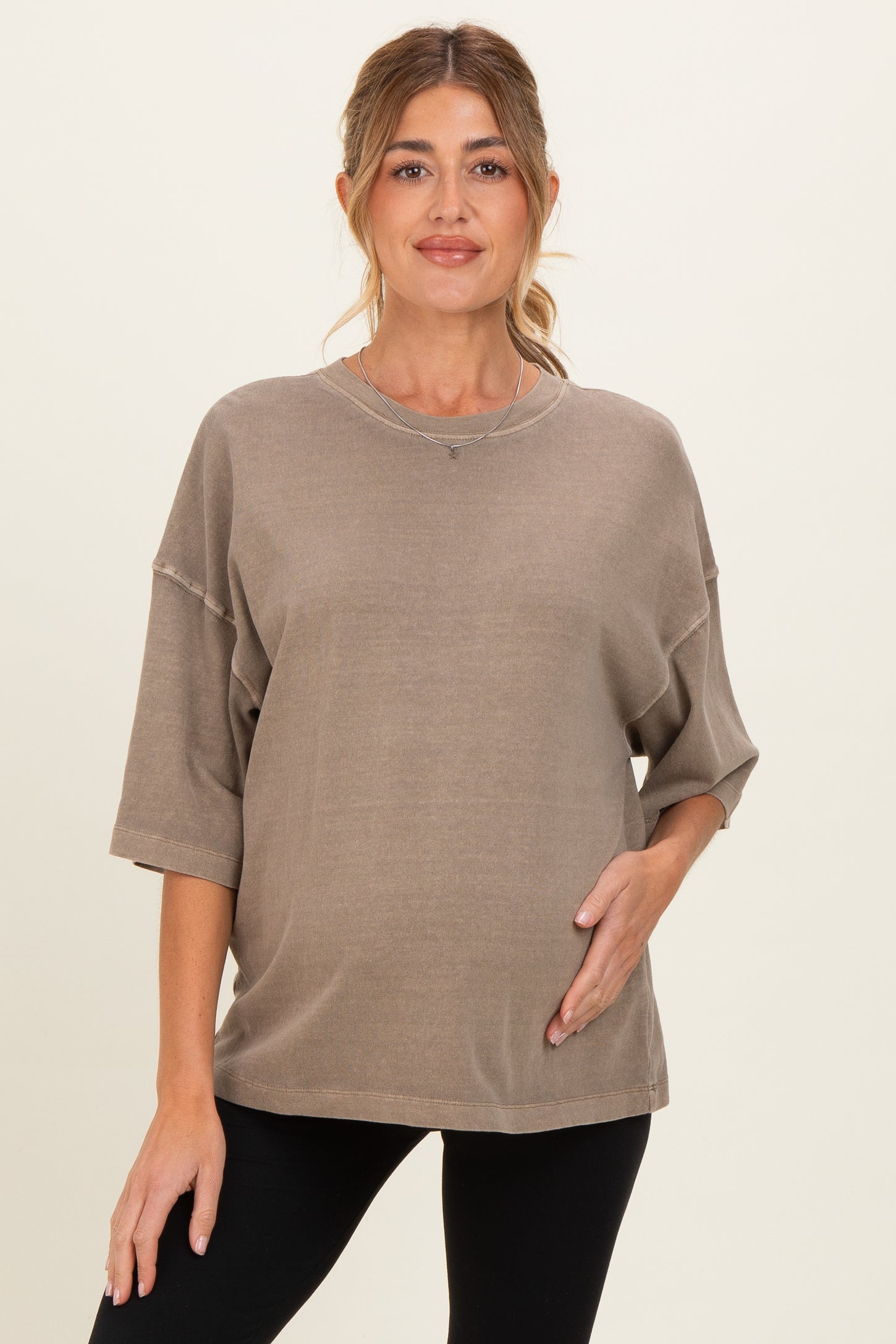 woman wearing a taupe oversized maternity sweatshirt and gently holding her baby bump