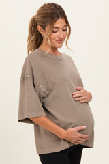 woman wearing a brown oversized maternity t-shirt, gently cradling her baby bump with a relaxed smile