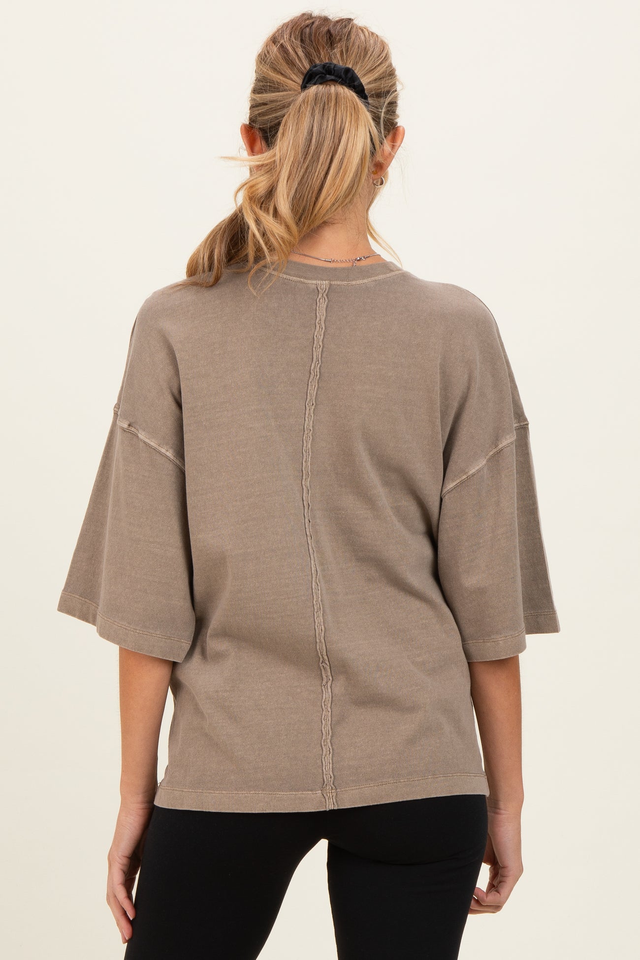 woman wearing a taupe oversized maternity top with short sleeves and back seam detail
