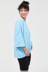 woman wearing a light blue oversized t-shirt and black bike shorts, smiling and facing slightly to the side