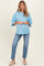 woman wearing a light blue oversized maternity top and distressed jeans, showing her baby bump