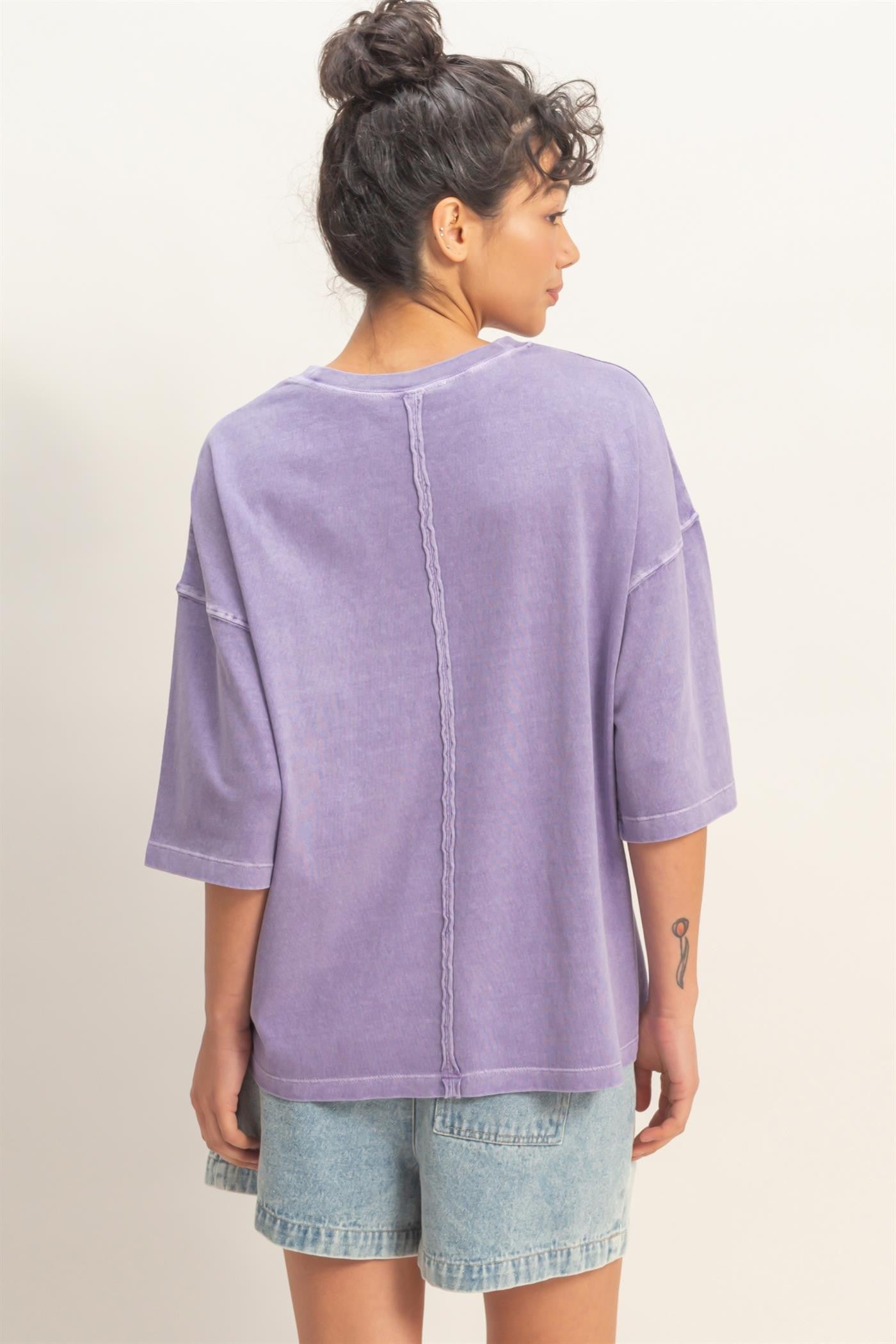 woman wearing a loose-fitting lavender purple oversized t-shirt and denim shorts, viewed from the back