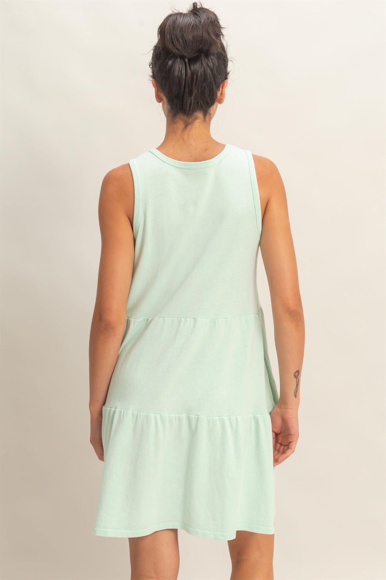woman wearing a mint green sleeveless tiered mini dress, viewed from the back