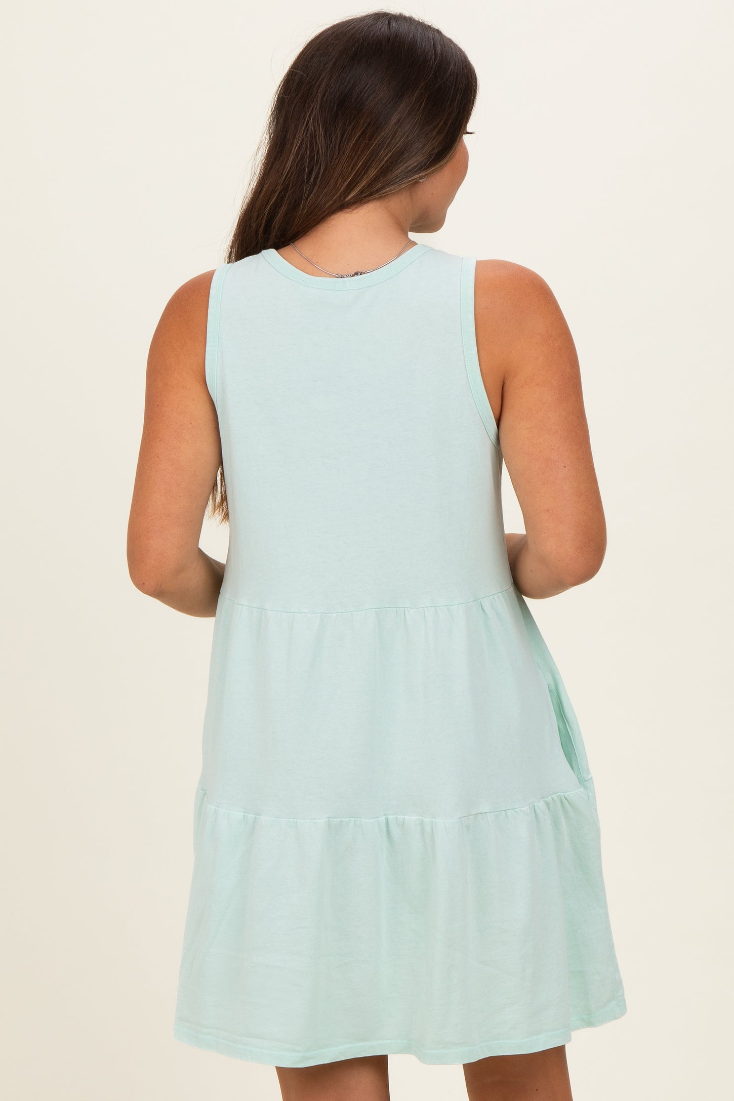woman wearing a mint green sleeveless maternity dress with a tiered skirt, showing the back view