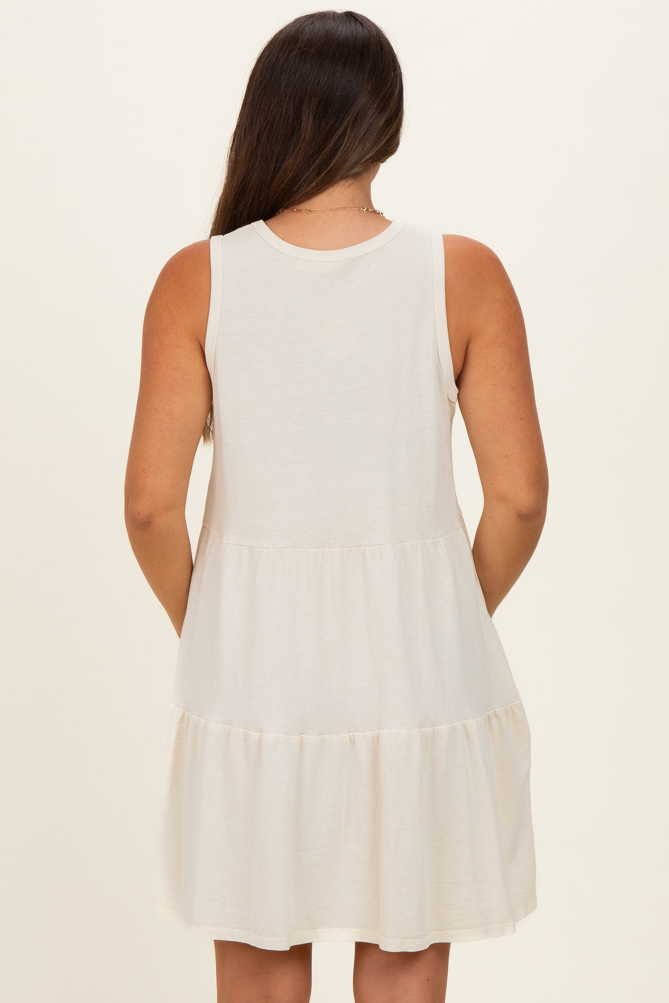 woman wearing a cream maternity dress with a tiered skirt and a sleeveless design, showing her back