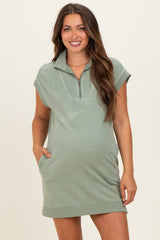 woman wearing a green short sleeve maternity dress with a zippered collar and side pockets, showcasing her baby bump