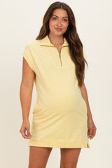 woman wearing a light yellow maternity zip-up dress with short sleeves and side slits showing her baby bump