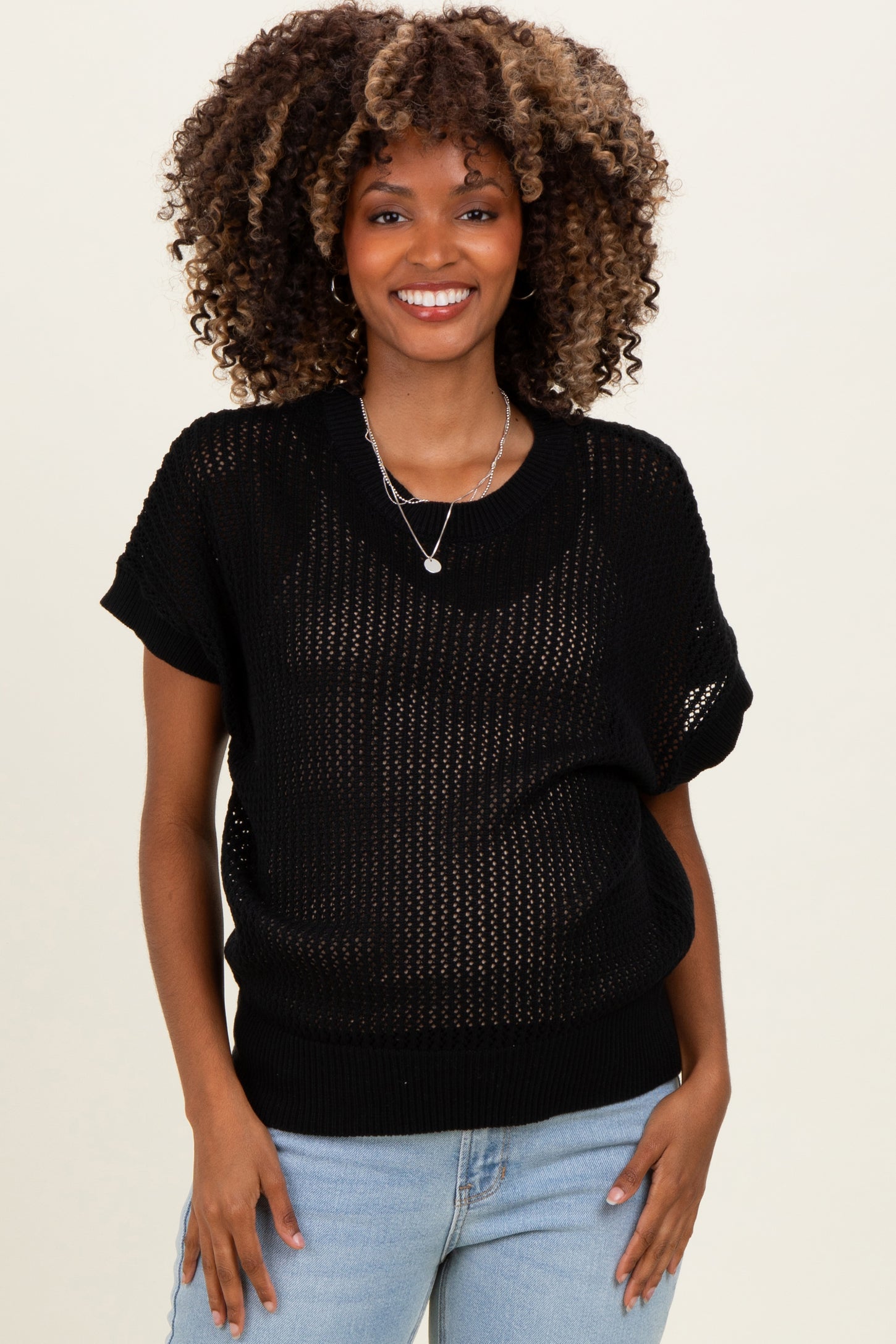 woman wearing a black open-knit maternity sweater with short sleeves and a relaxed fit, smiling at the camera