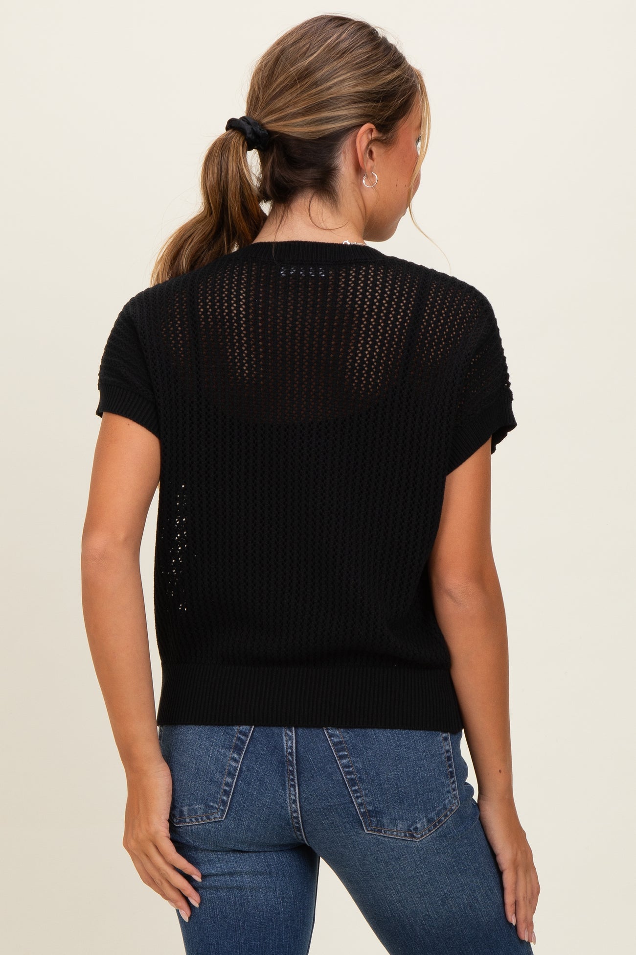 woman wearing a black short sleeve knitted sweater with a loose fit, shown from the back with blue jeans