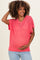 woman wearing a coral open-knit maternity top and holding her baby bump