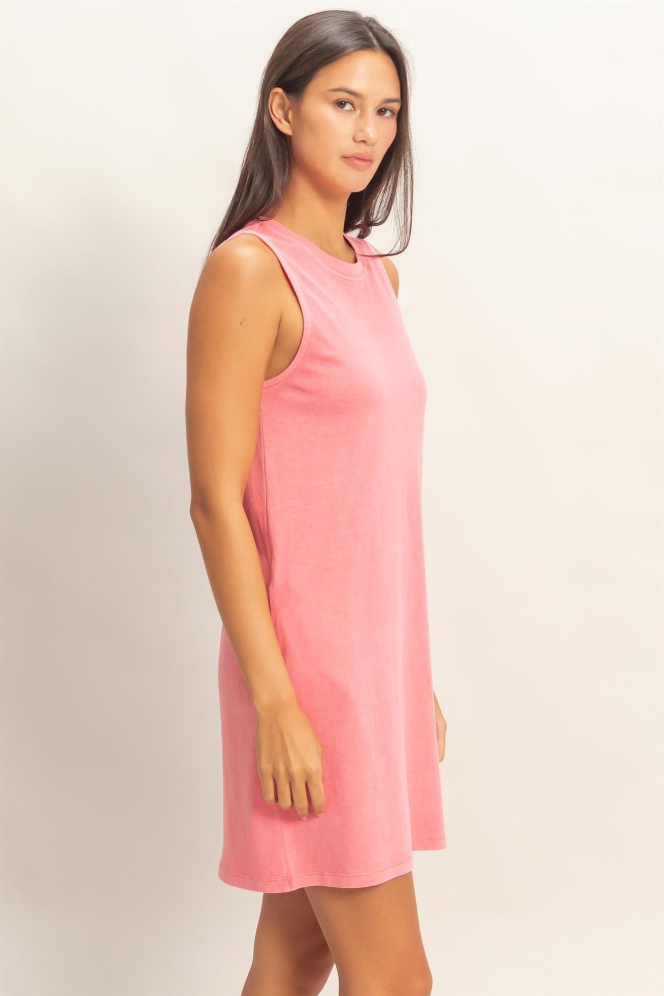 woman wearing a coral pink sleeveless casual dress, standing sideways with a relaxed fit