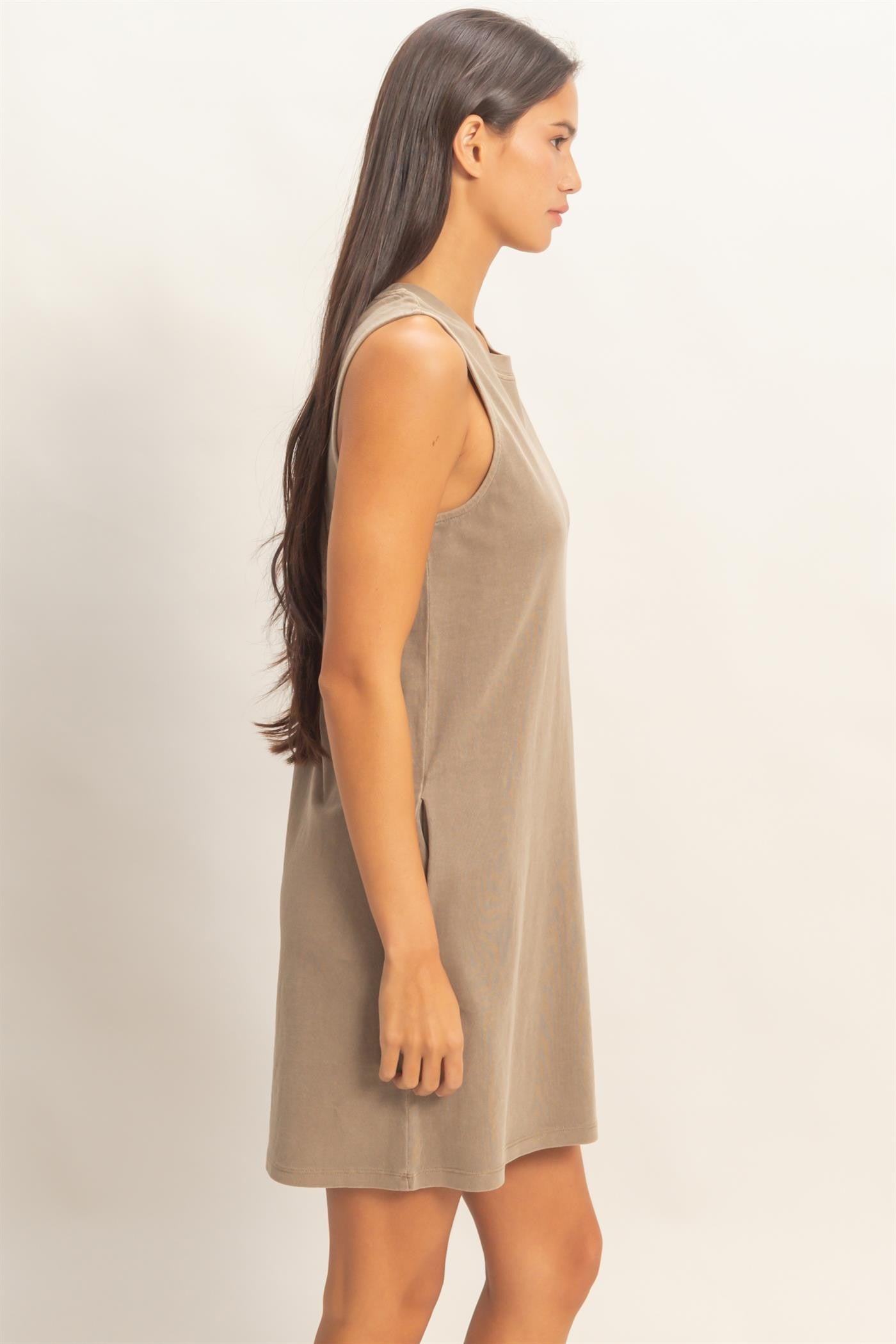 woman wearing a tan sleeveless mini dress with a relaxed fit and side pockets, shown from the side