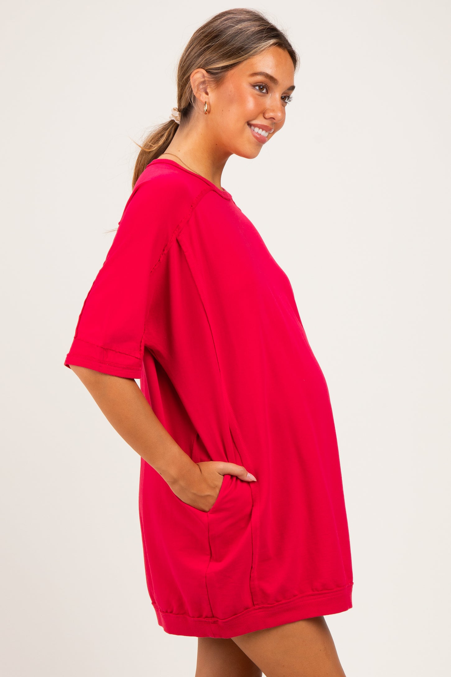 woman wearing a bright red oversized maternity dress with side pockets and a visible baby bump