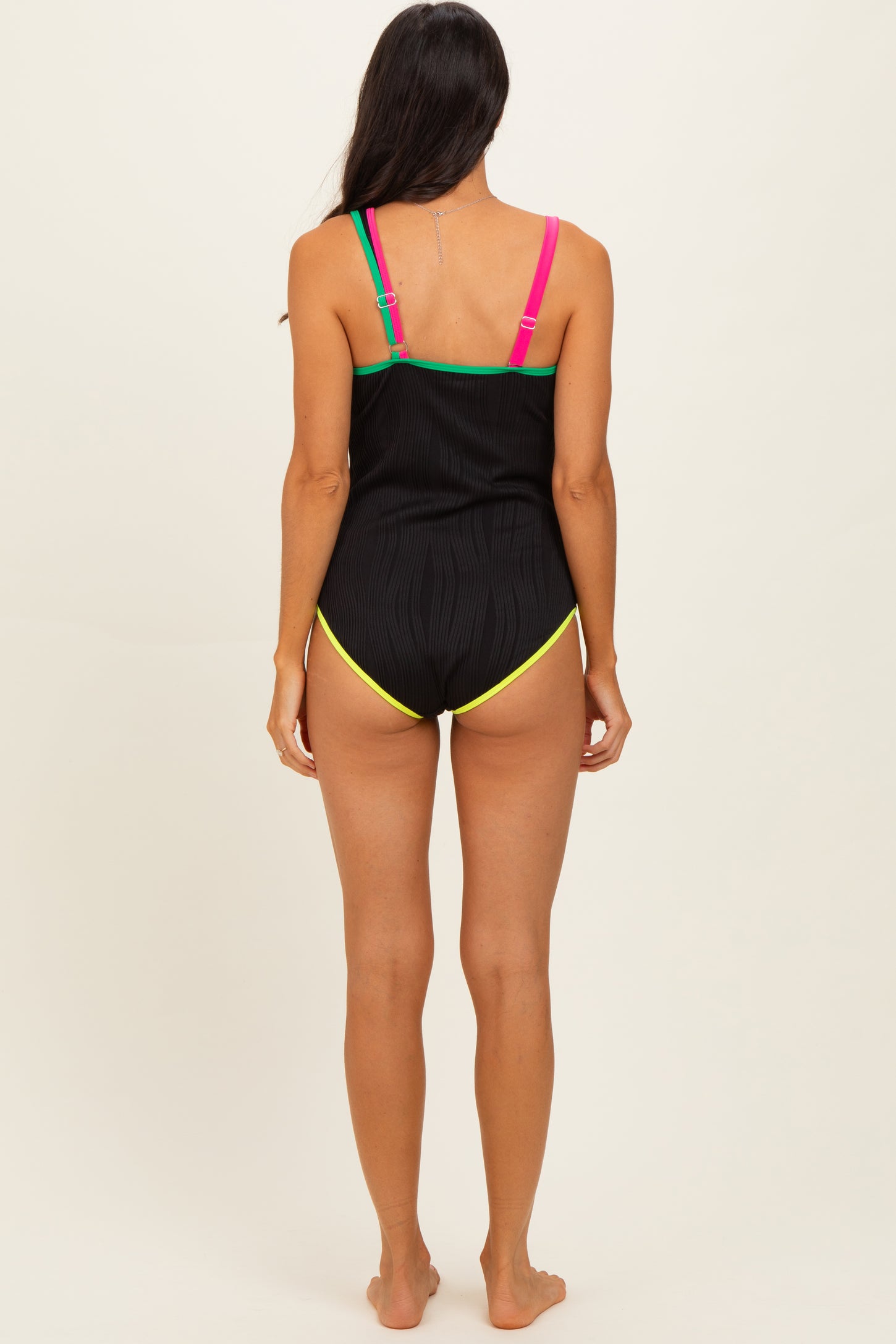 woman wearing a black ribbed swimsuit with colorful straps and a low-cut back