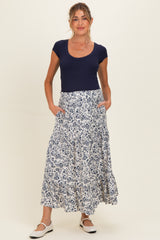 woman wearing a navy blue scoop neck maternity top and a white floral print tiered maternity maxi skirt with pockets