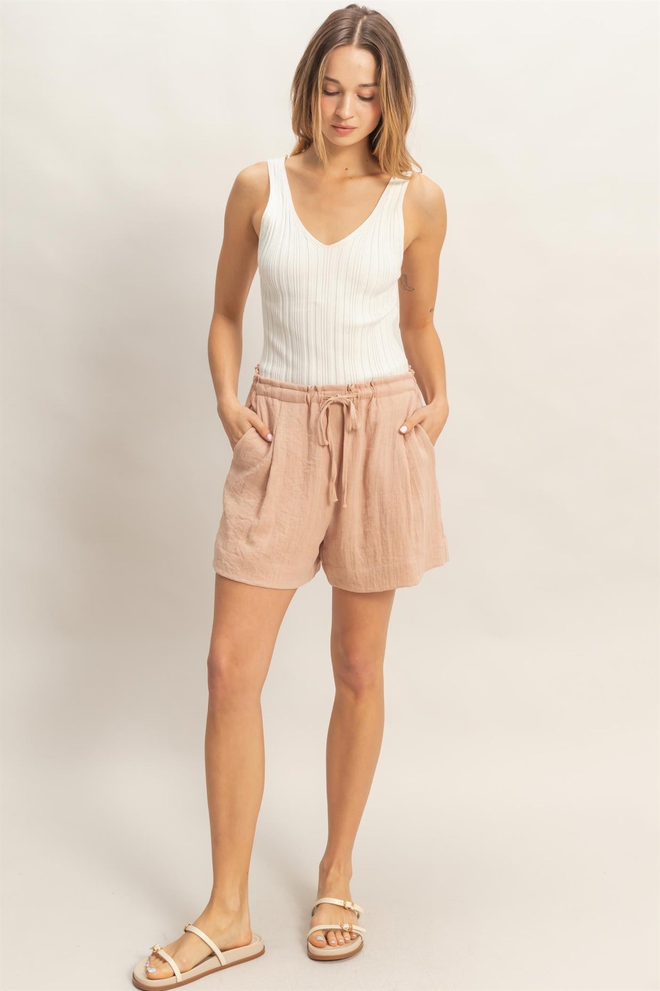 woman wearing a white sleeveless ribbed top and light pink drawstring linen shorts