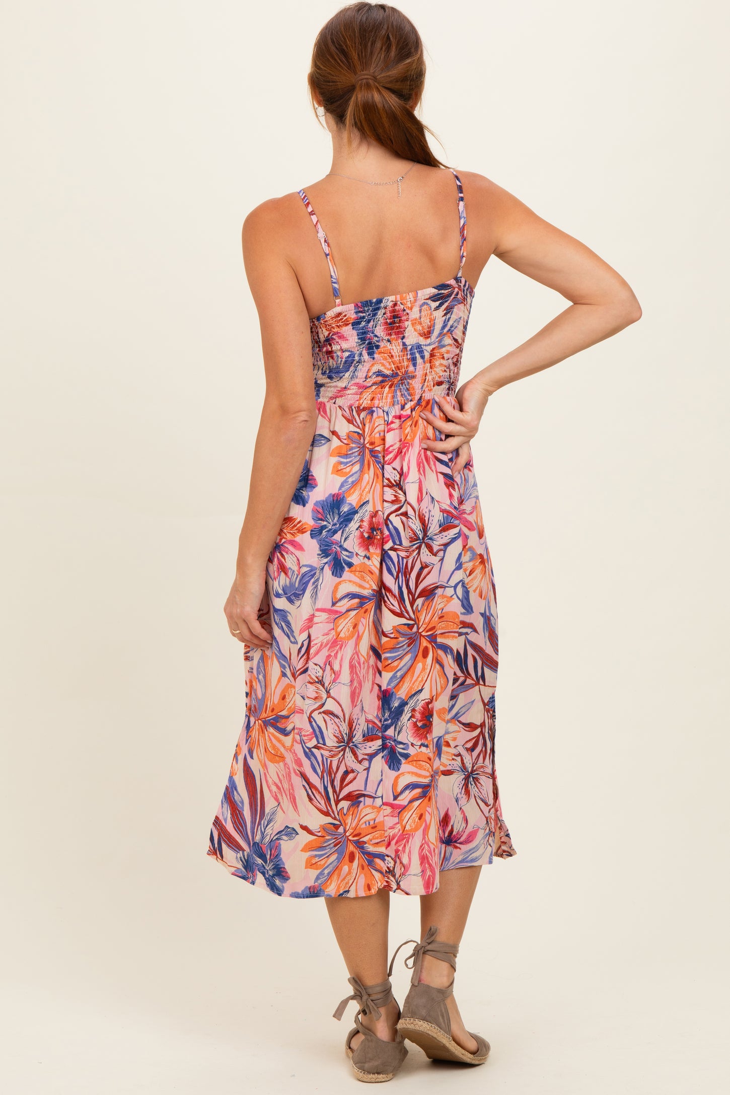 woman wearing a back view of a floral print smocked midi dress with adjustable straps and a flared skirt