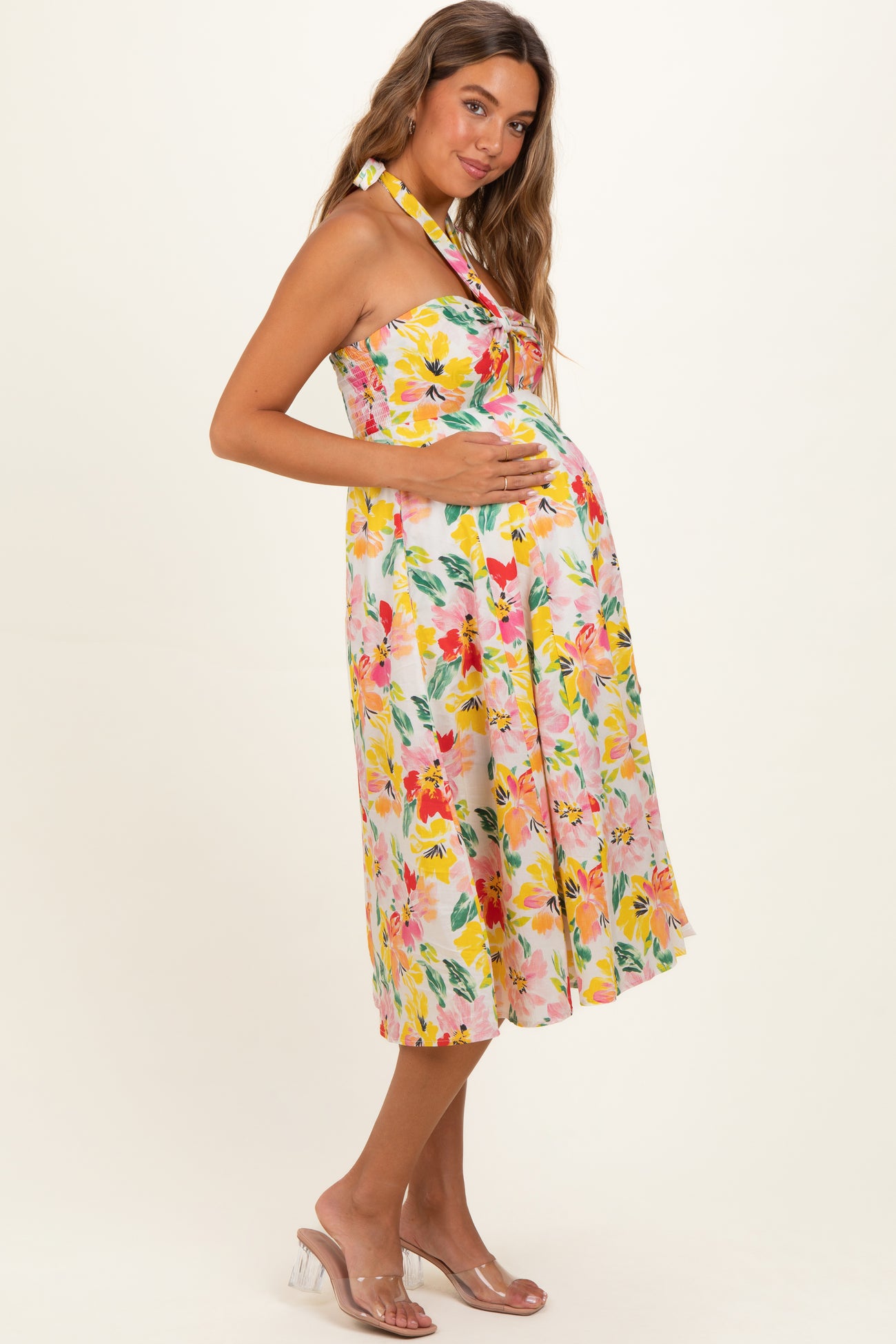 woman wearing a floral midi maternity dress with a halter neckline and holding her baby bump