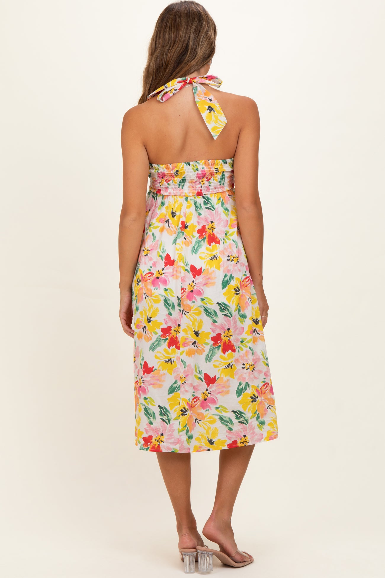 woman wearing a floral maternity dress with a back tie and smocked bodice, featuring bright colors and a midi length