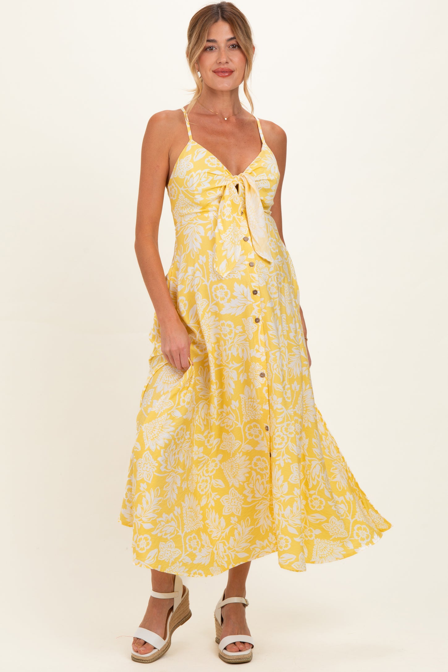 woman wearing a yellow floral maternity dress with a tie front and buttons, showcasing her baby bump