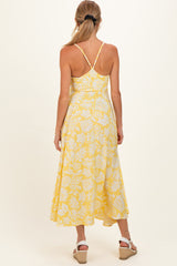 woman wearing a yellow floral print maternity dress with a flowing skirt and adjustable straps, showing her back
