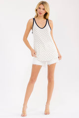 woman wearing a white sleeveless tank top with navy dots and trim, paired with distressed white shorts
