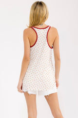woman wearing a white tank top with red floral pattern and red trim, paired with distressed white shorts