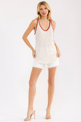 woman wearing a cream tank top with red polka dots and red trim, paired with white denim shorts and clear heels