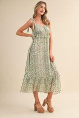 woman wearing a green floral maxi dress with ruffled details and tied straps, standing in a neutral background