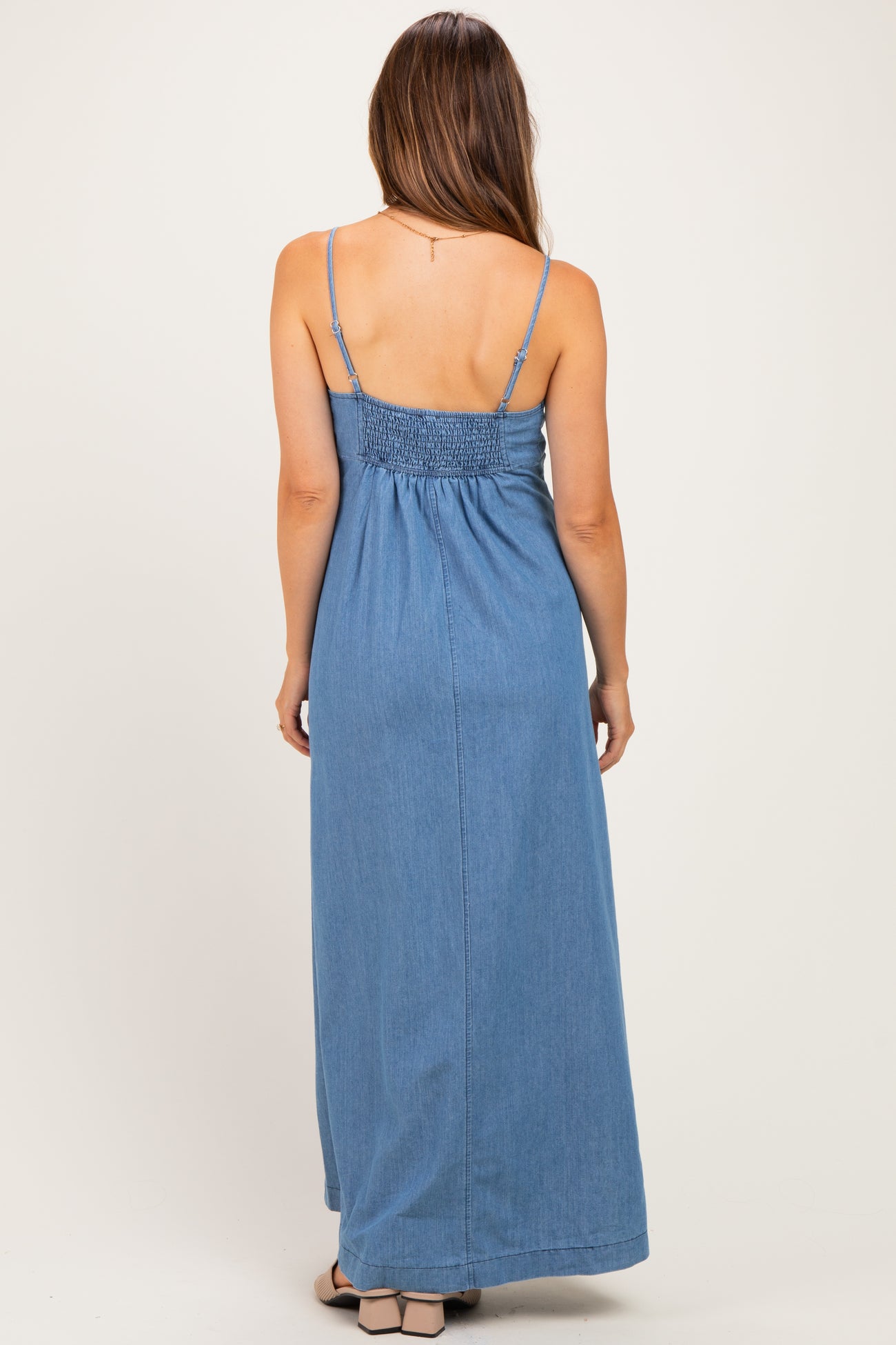 woman wearing a denim maxi maternity dress with smocked back and adjustable straps, viewed from the back