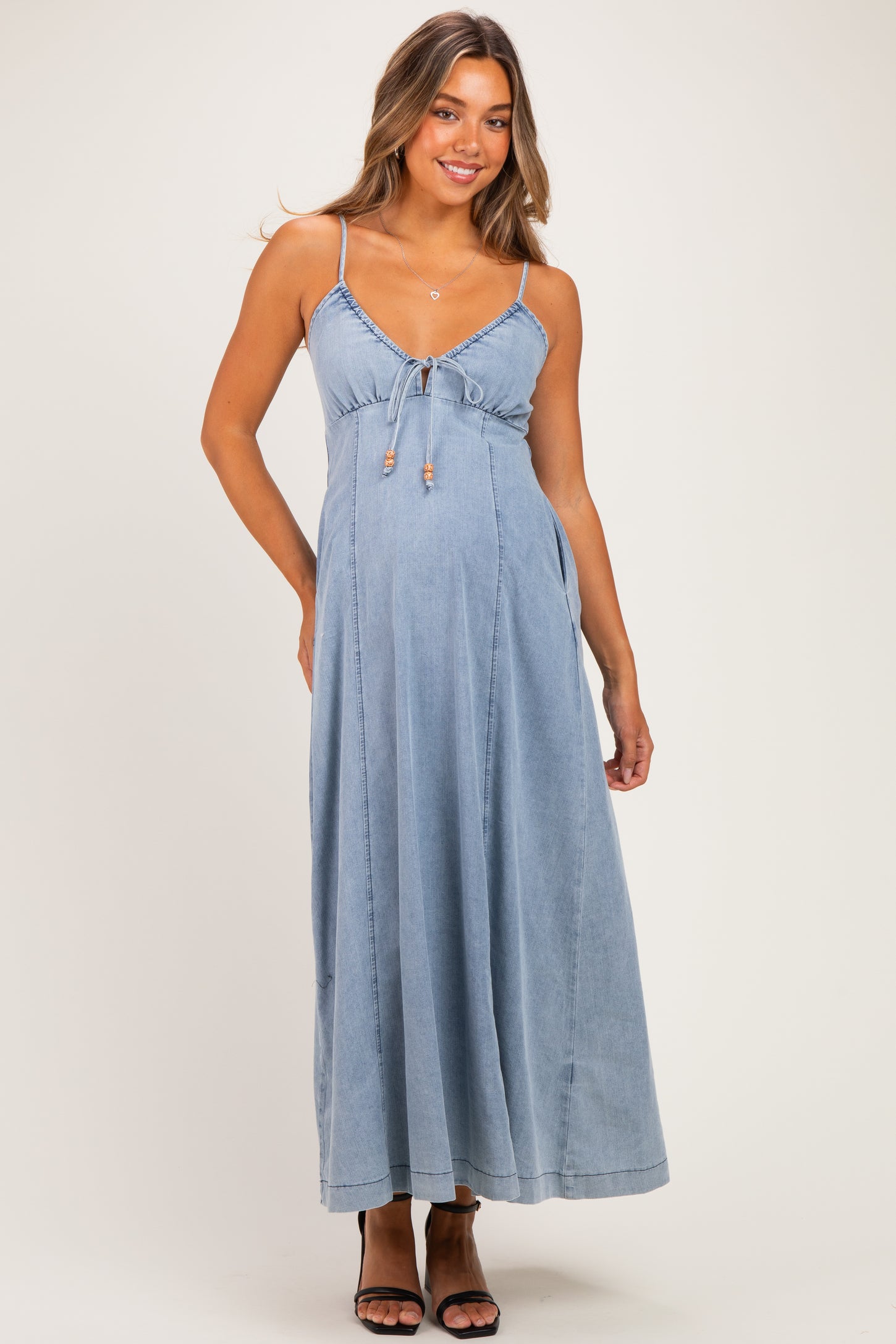 woman wearing a light blue maternity maxi dress with adjustable straps and a tie detail at the bust, showing her baby bump