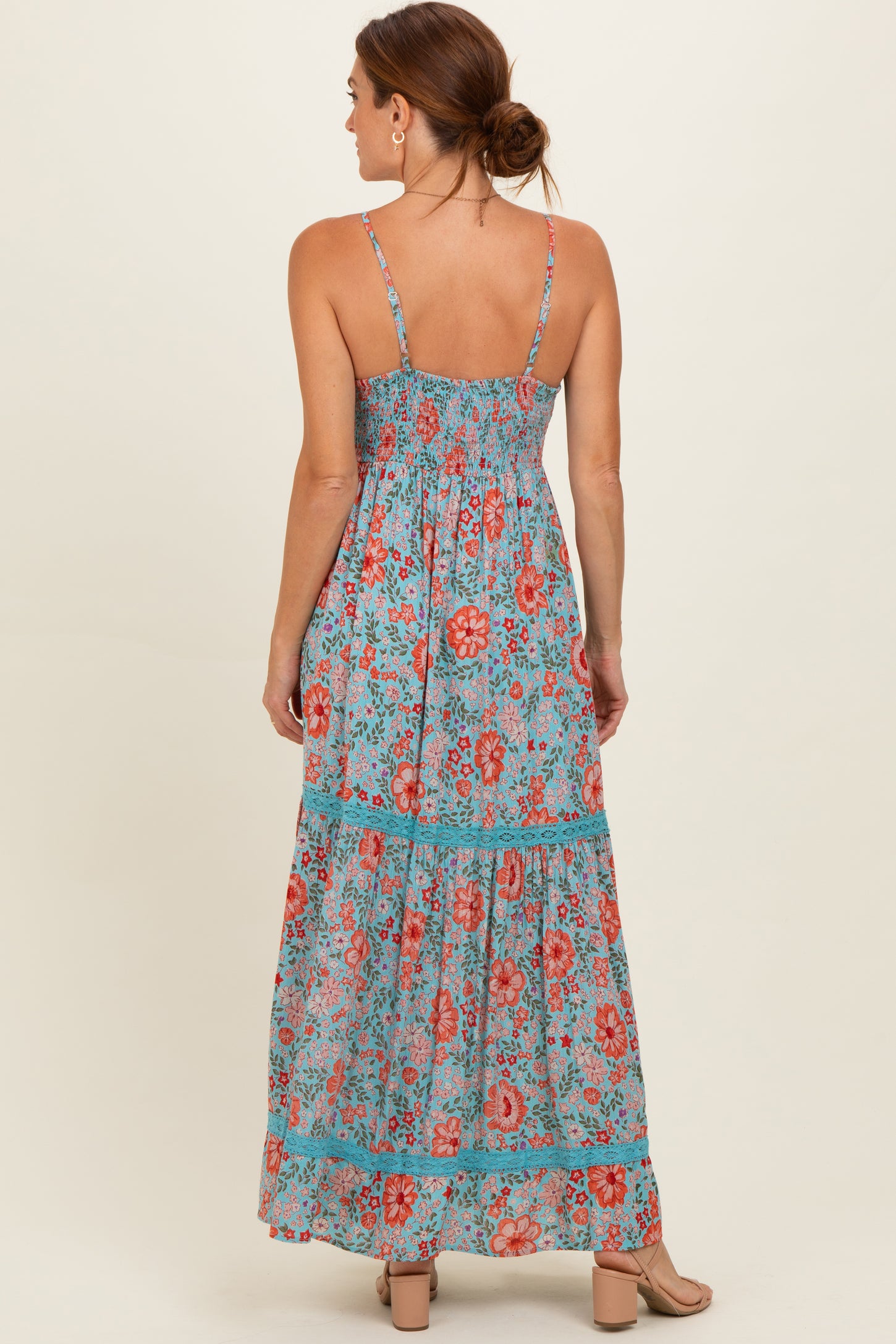 woman wearing a sleeveless maxi dress with a floral print in shades of blue, red, and green, showing a tiered design from the back