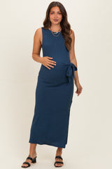 woman wearing a navy blue sleeveless maternity maxi dress with a side tie and holding her baby bump