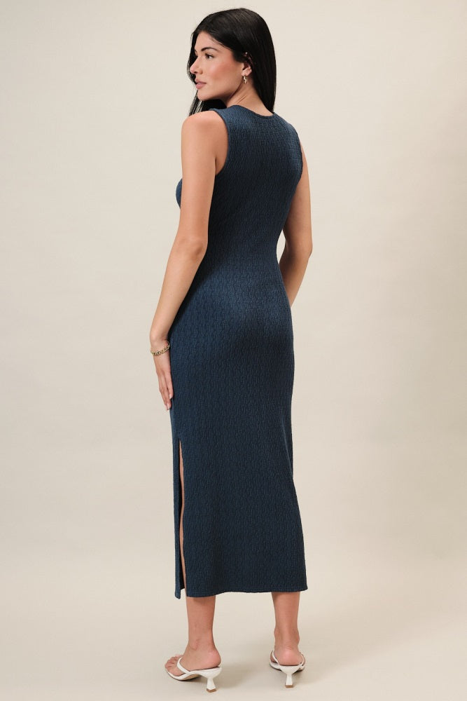 woman wearing a navy blue sleeveless midi dress with a side slit, standing turned to the side