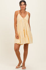 woman wearing a light yellow sleeveless mini dress with eyelet detailing and a tie front, standing against a neutral background