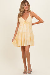 woman wearing a yellow maternity dress with a tie front and tiered skirt, showcasing her baby bump