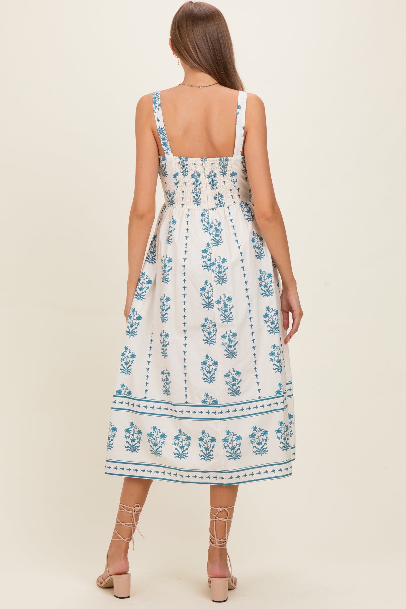 woman wearing a white floral print maternity dress with blue details, showing the back and adjustable straps
