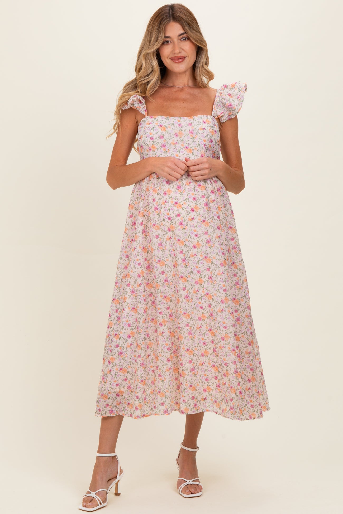 woman wearing a floral maternity dress with a square neckline and flutter sleeves, standing and smiling