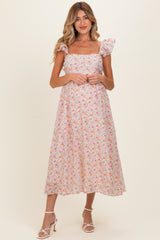 woman wearing a floral maternity dress with a square neckline and flutter sleeves, standing and smiling