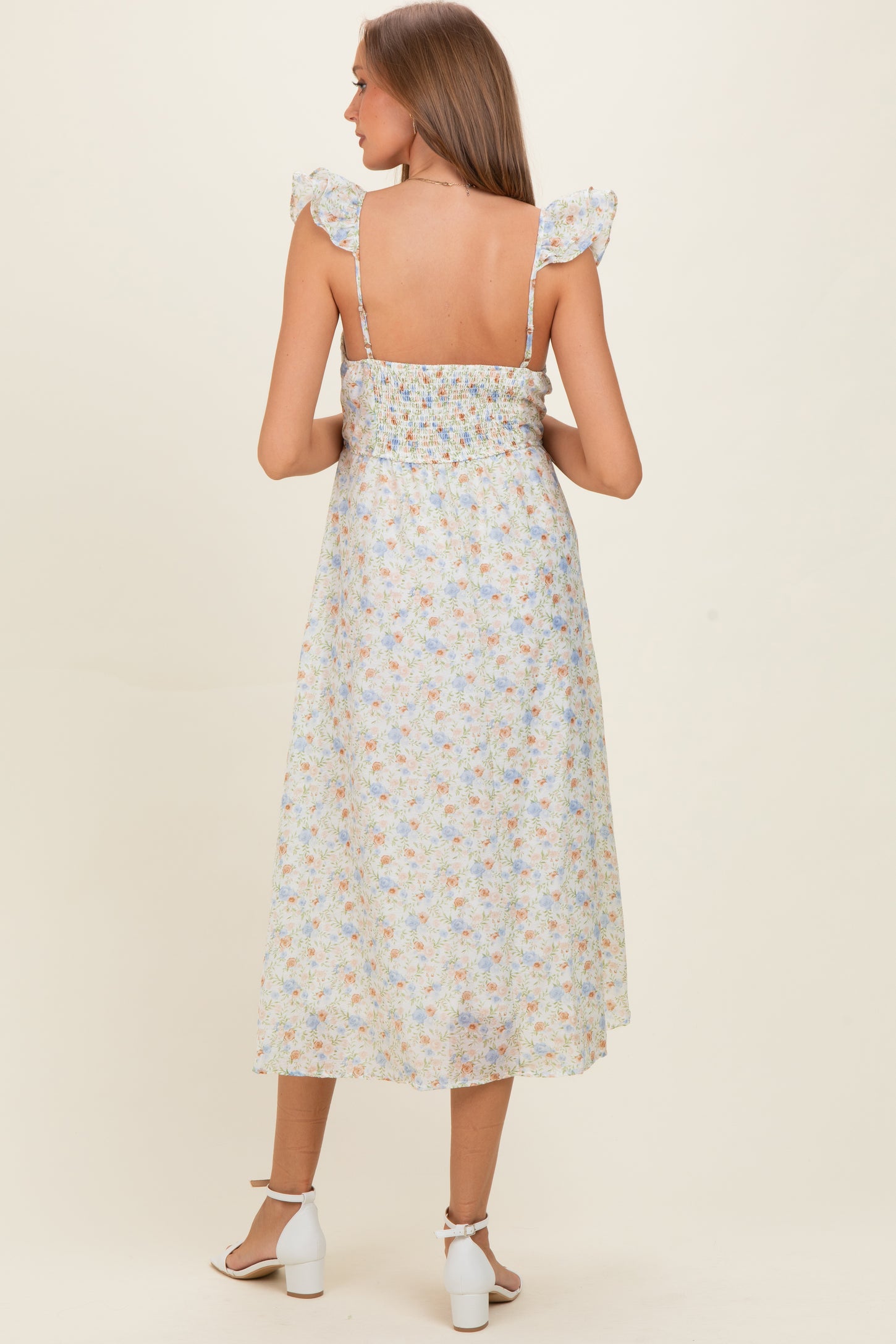 woman wearing a light floral print maternity dress with ruffled straps and a smocked bodice, showing her back