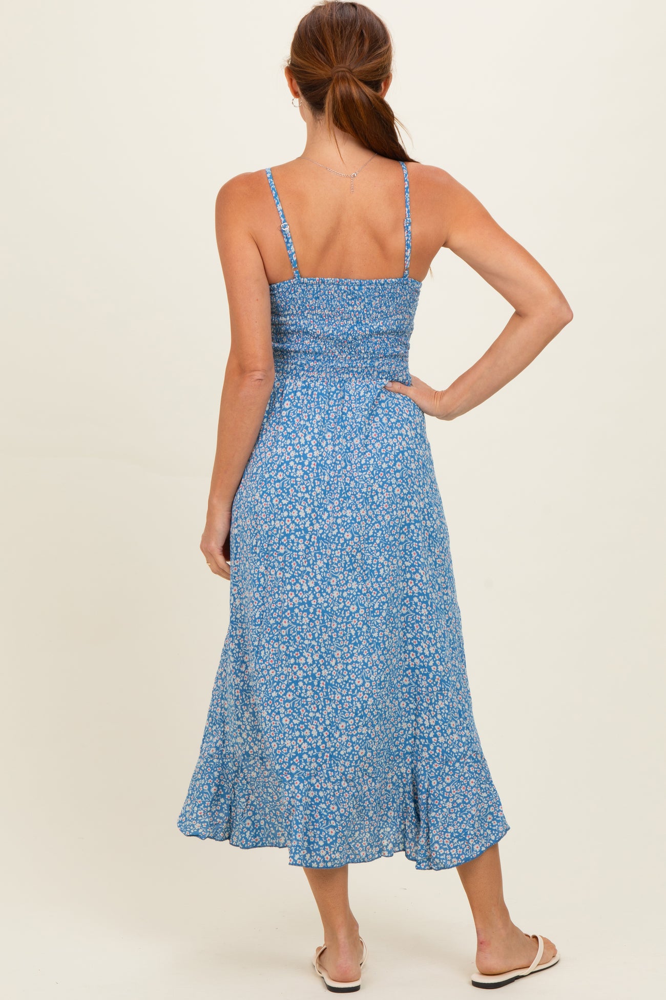 woman wearing a blue floral midi dress with adjustable straps and a smocked back, shown from the back