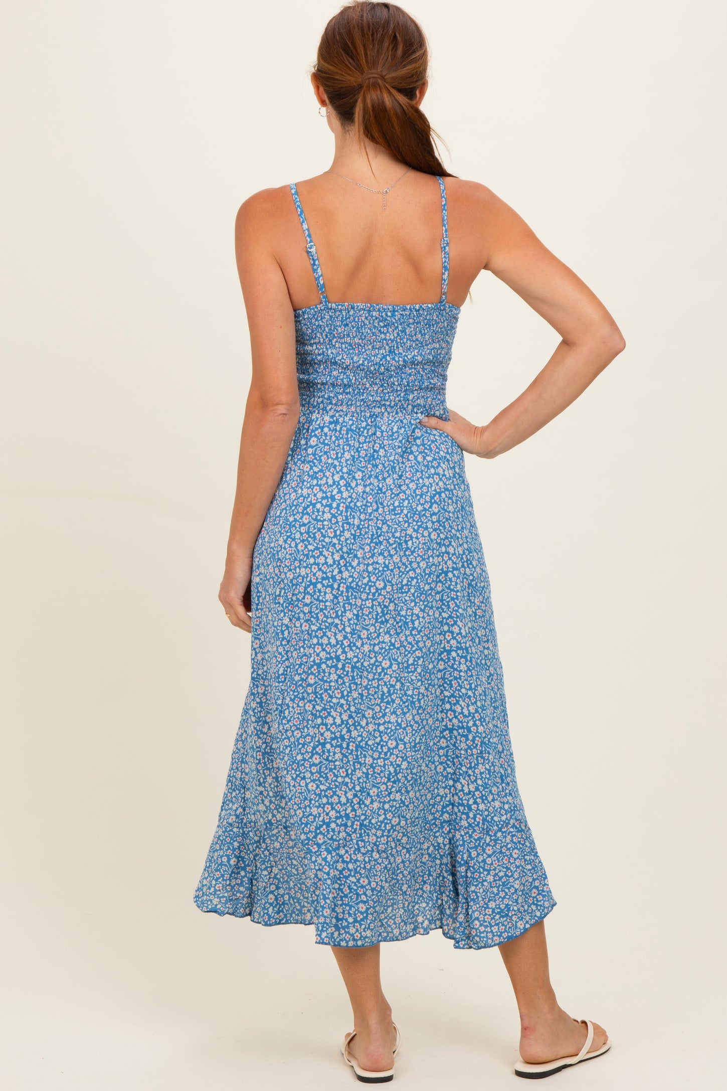 woman wearing a blue floral midi dress with adjustable straps and a smocked back, shown from the back