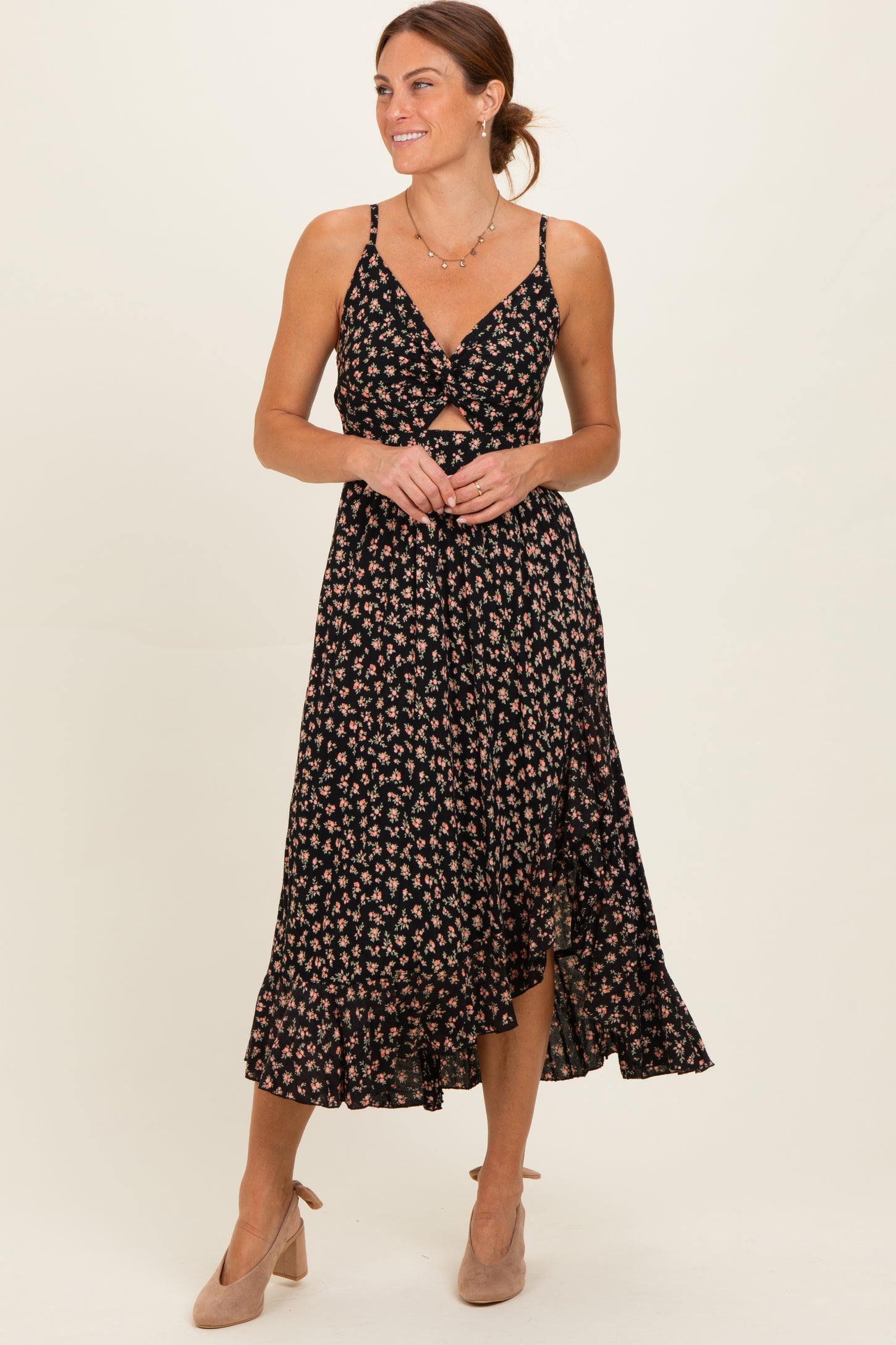 woman wearing a black floral midi dress with a front twist detail and spaghetti straps, paired with nude heels